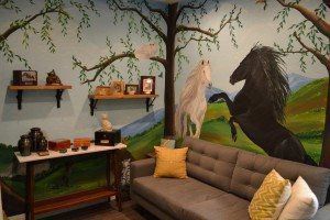 room with shelves on the wall, a gray couch, and a painted horse mural
